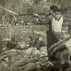 Vtg Old Candid Snapshot Photo Woman Shooting Rifle Man Sitting On Rocks By River